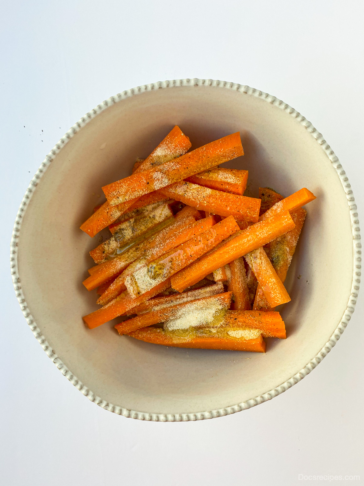Overhead image of Air Fryer Carrot fries uncooked in bowl with seasoning