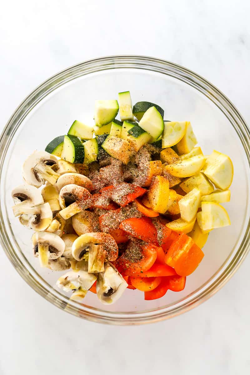Seasoned chopped uncooked veggies in a round glass bowl.
