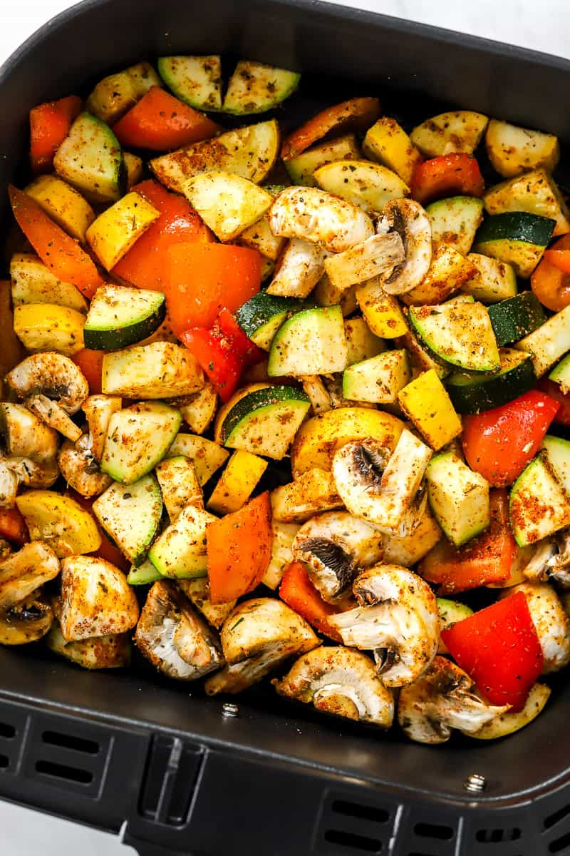 Seasoned, uncooked chopped veggies in a black air fryer basket.