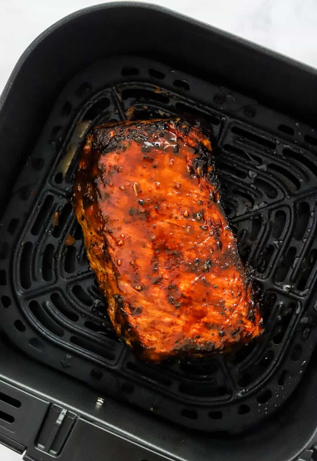 Cooked pork in a black air fryer basket.