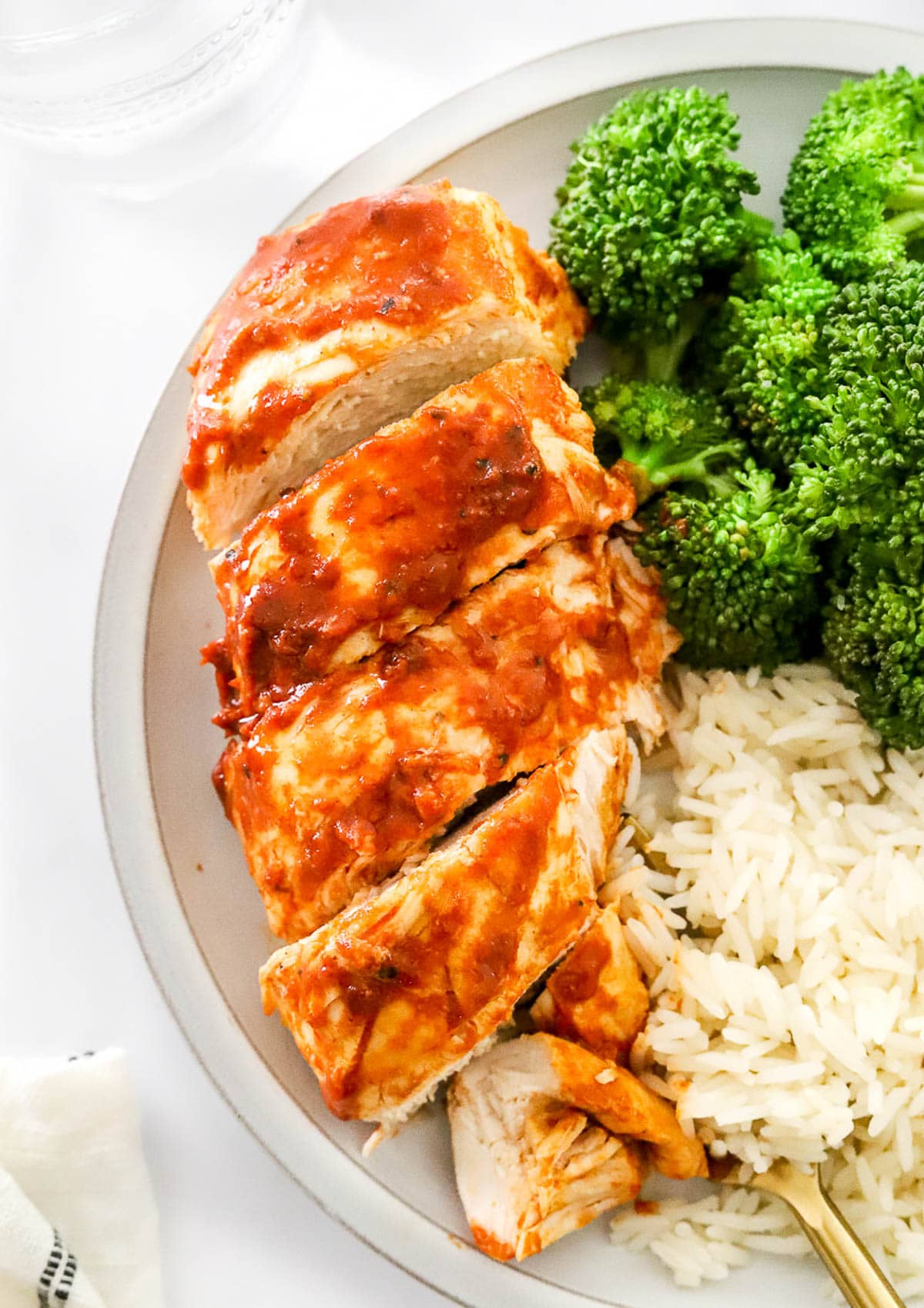 Sliced BBQ chicken breast served with white rice and steamed broccoli on a plate.