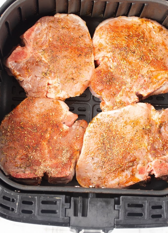 raw pork chops covered in seasoning in air fryer basket