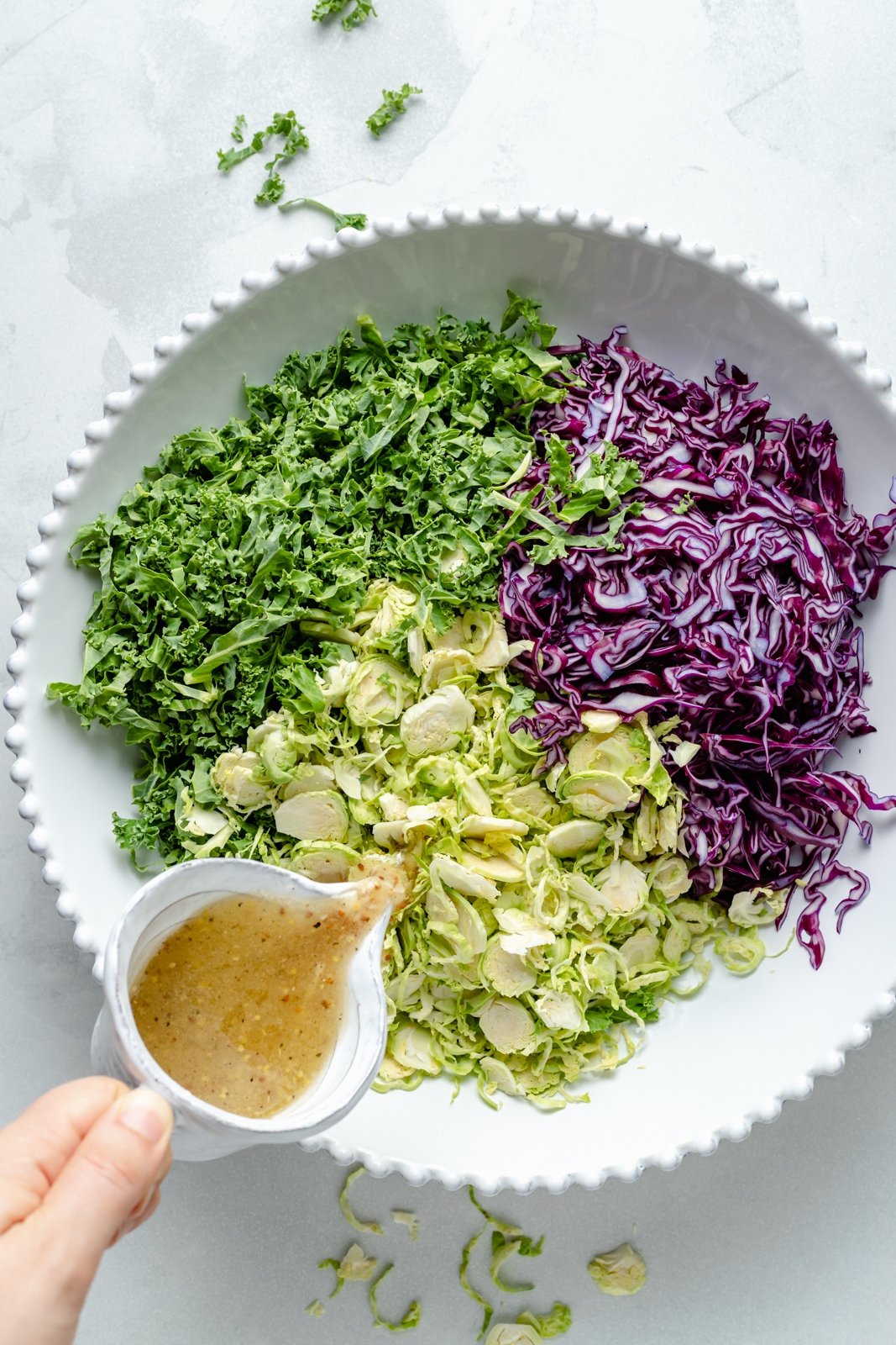 pouring maple cider dressing into a bowl of brussels sprouts, kale and cabbage