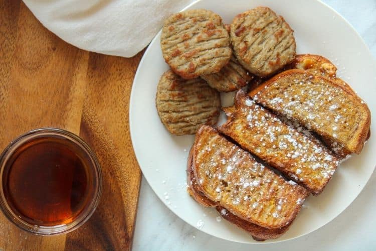 Air Fryer French Toast Sticks and Sausage on a white plate with a bowl of maple syrup to the side