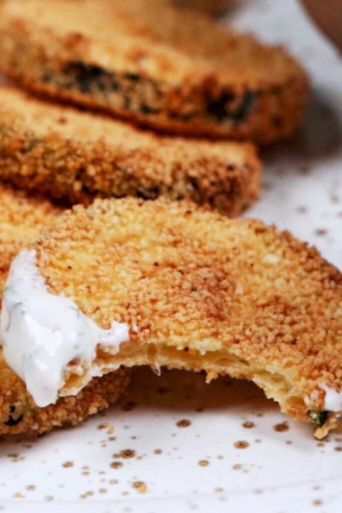 Close up of air fried zucchini chip with a bite taken out of it and dip on it