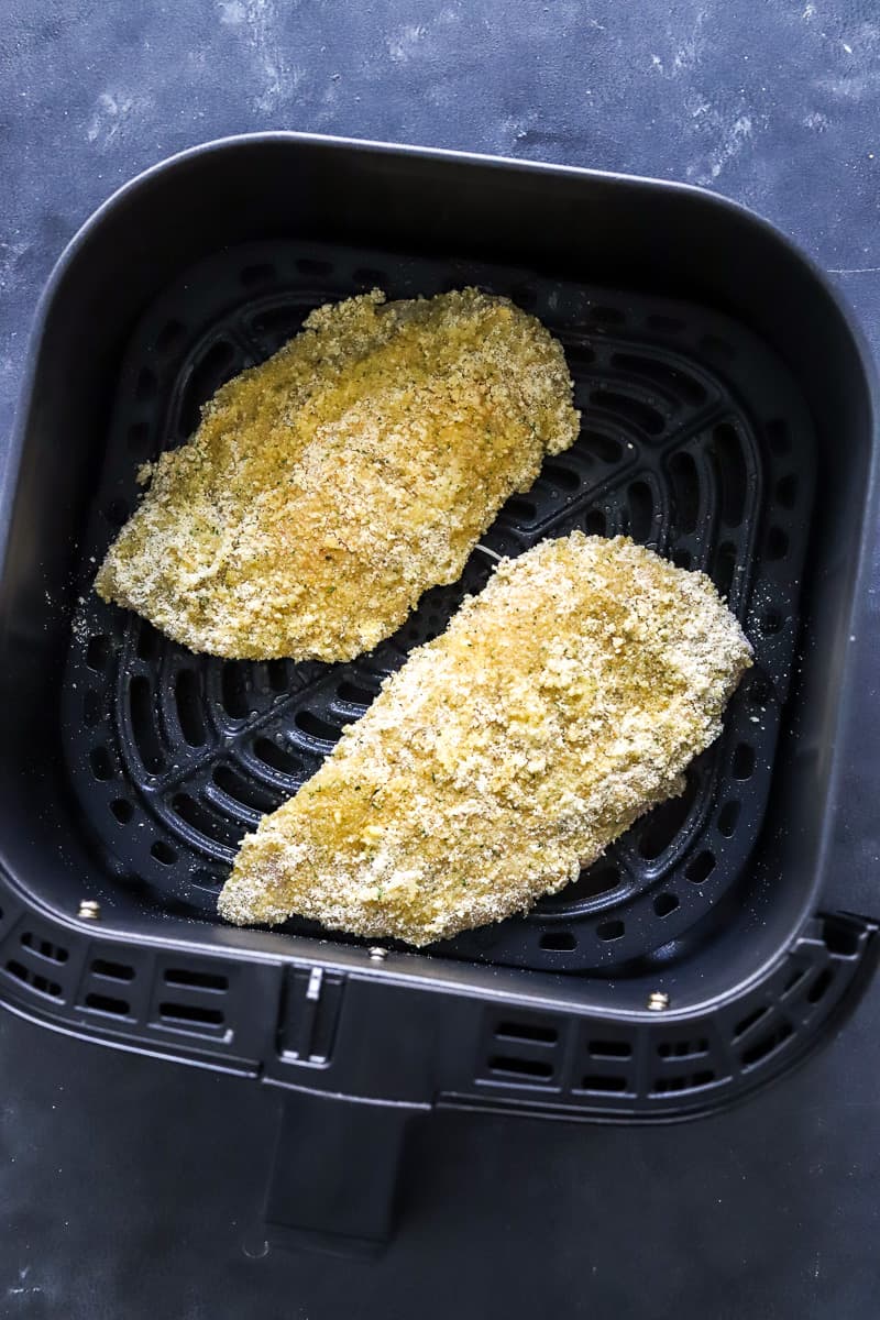 Uncooked, breaded chicken cutlets on a square, black air fryer basket.