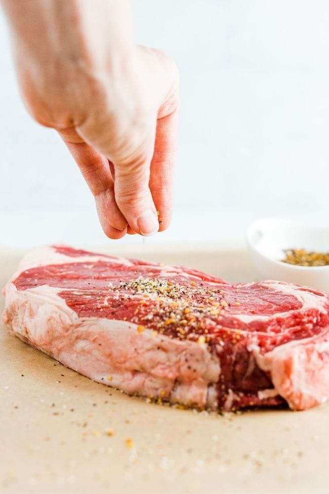 Raw steak being seasoned