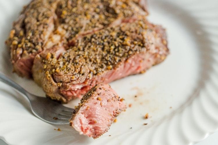 Cut ribeye steak cooked to medium rare with a bite-sized piece on a fork (on a white plate)