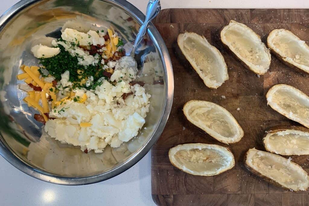 baked potatoes scooped into a bowl with butter, cheddar, cooked bacon, and parsley