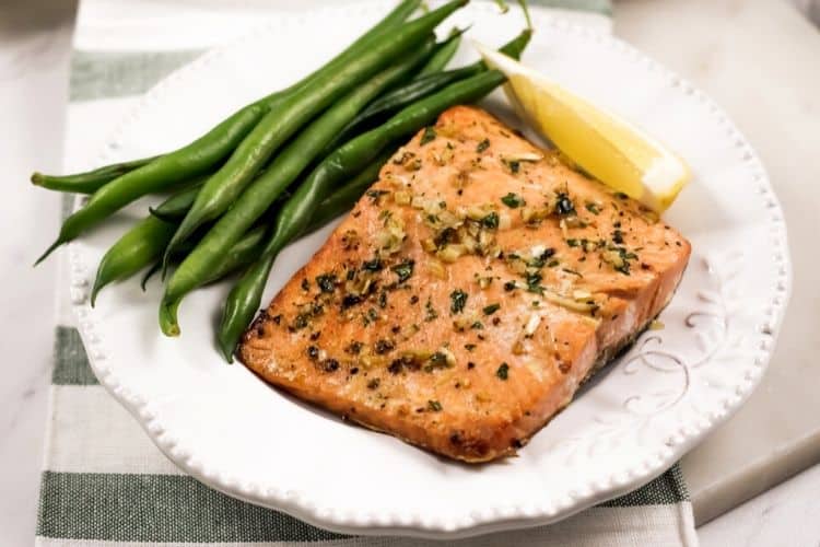 Garlic Salmon on a white plate with green beans and a lemon