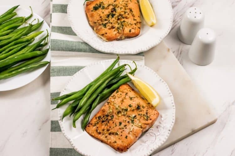 Wide angle view of a marble counter with garlic salmon and green beans on a white plate with a grey and white table runner in the middle