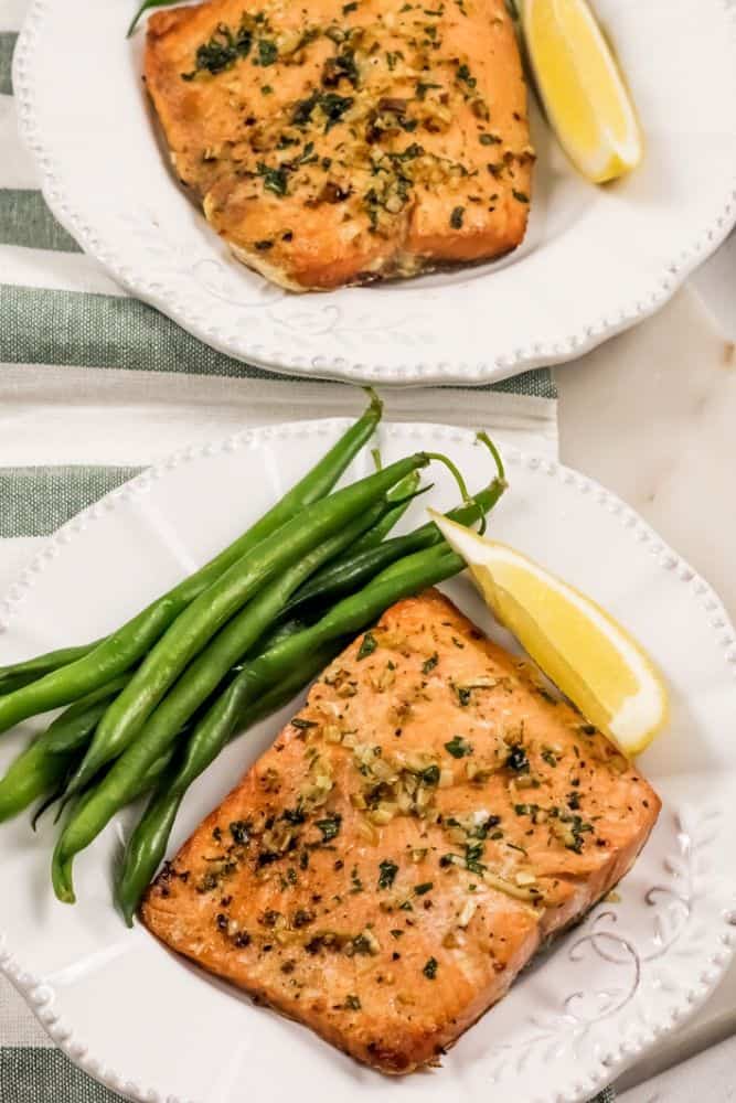 Vertical image of Air Fryer Garlic Salmon on a white plate with green beans and a lemon