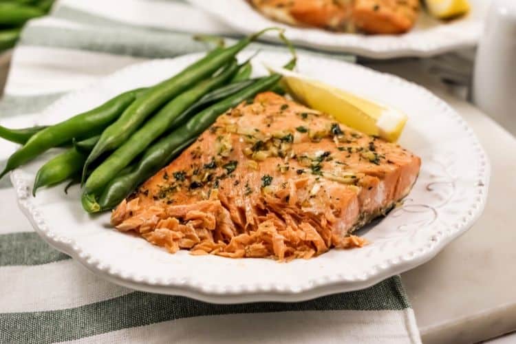 Garlic Butter Salmon that is shown flaking on a white plate with green beans and a lemon