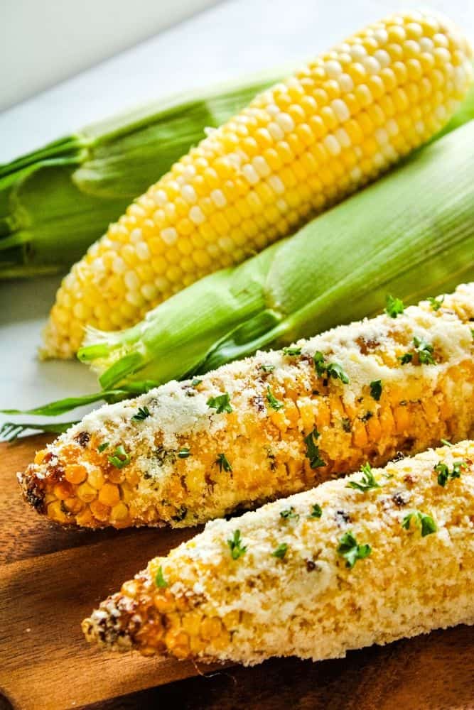 Air fryer corn on the cob with parmesan on a cutting board with more corn in the background