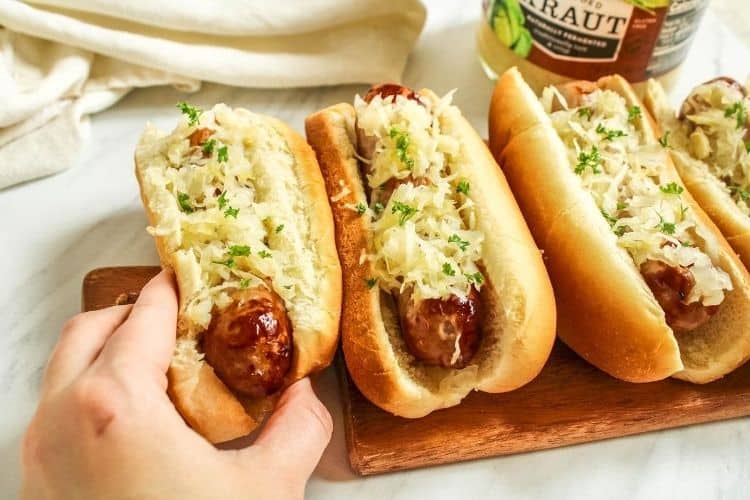 Air Fryer Brats in buns with sauerkraut on top and hand grabbing one