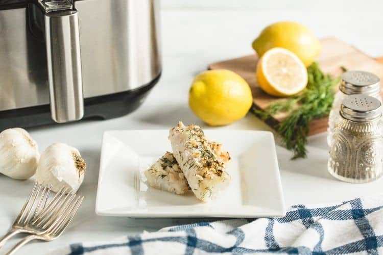 Air Fryer Cod on a white plate with ingredients and an air fryer in the background