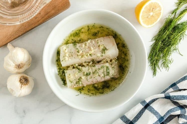 Cod inside a bowl with lemon, garlic, dill, and butter