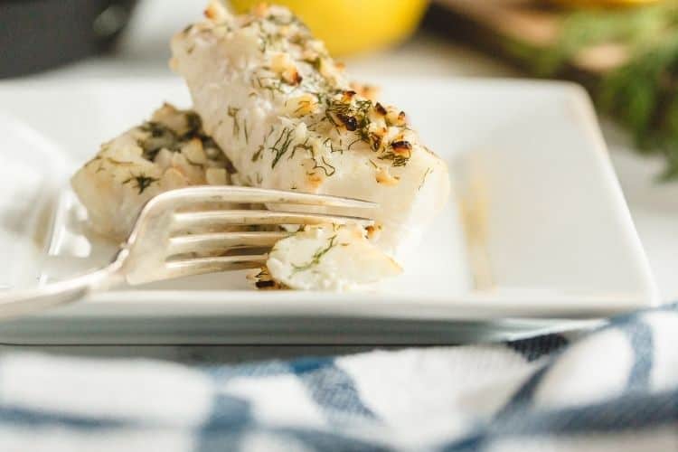 Air Fryer Cod on a white plate with a fork taking a bite out of the cod loin