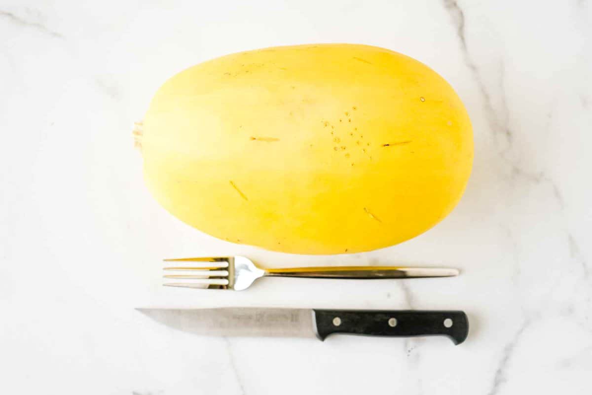 whole spaghetti squash on a white marble background next to a fork and a knife.