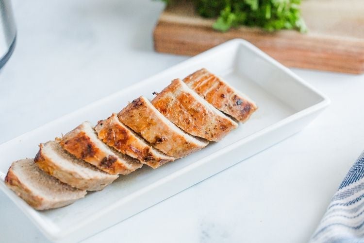 Pork tenderloin on a white serving plate sliced into coin-shaped pieces